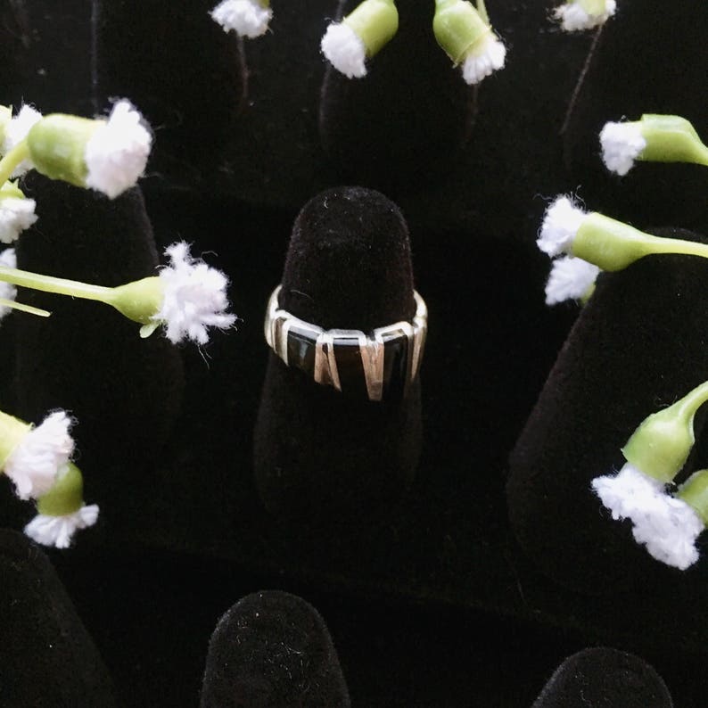 May include: A black and silver ring with a geometric design. The ring is on a black velvet display stand.