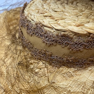 May include: A straw hat with a brown ribbon and lace trim. The hat is decorated with a brown feather.
