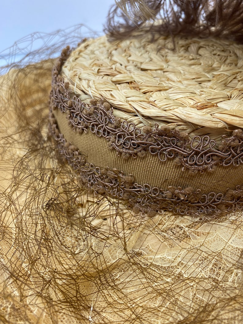 May include: A straw hat with a brown ribbon and lace trim. The hat is decorated with a brown feather.