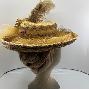 May include: A straw hat with a brown ribbon and a brown feather. The hat is on a mannequin head.