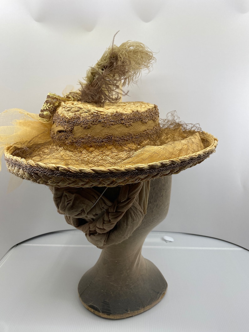 May include: A straw hat with a brown ribbon and a brown feather. The hat is on a mannequin head.