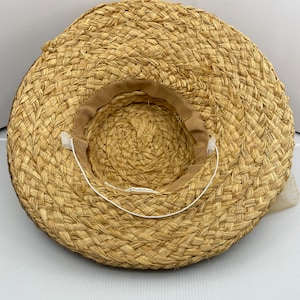 May include: A straw hat with a brown woven brim and a white ribbon tied around the crown.