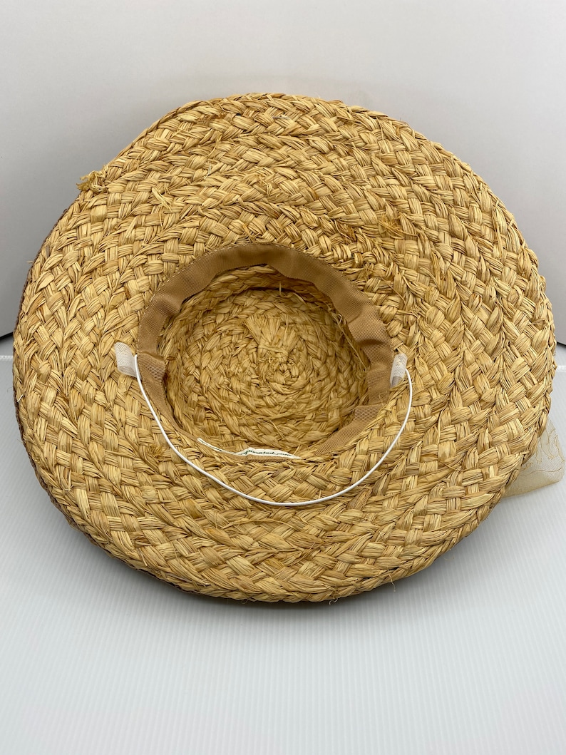 May include: A straw hat with a brown woven brim and a white ribbon tied around the crown.