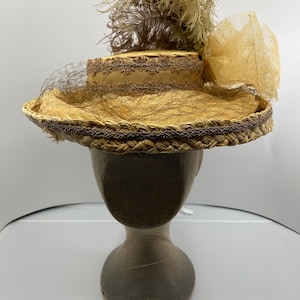 May include: A straw hat with a brown ribbon and a brown feather. The hat is on a wooden hat form.