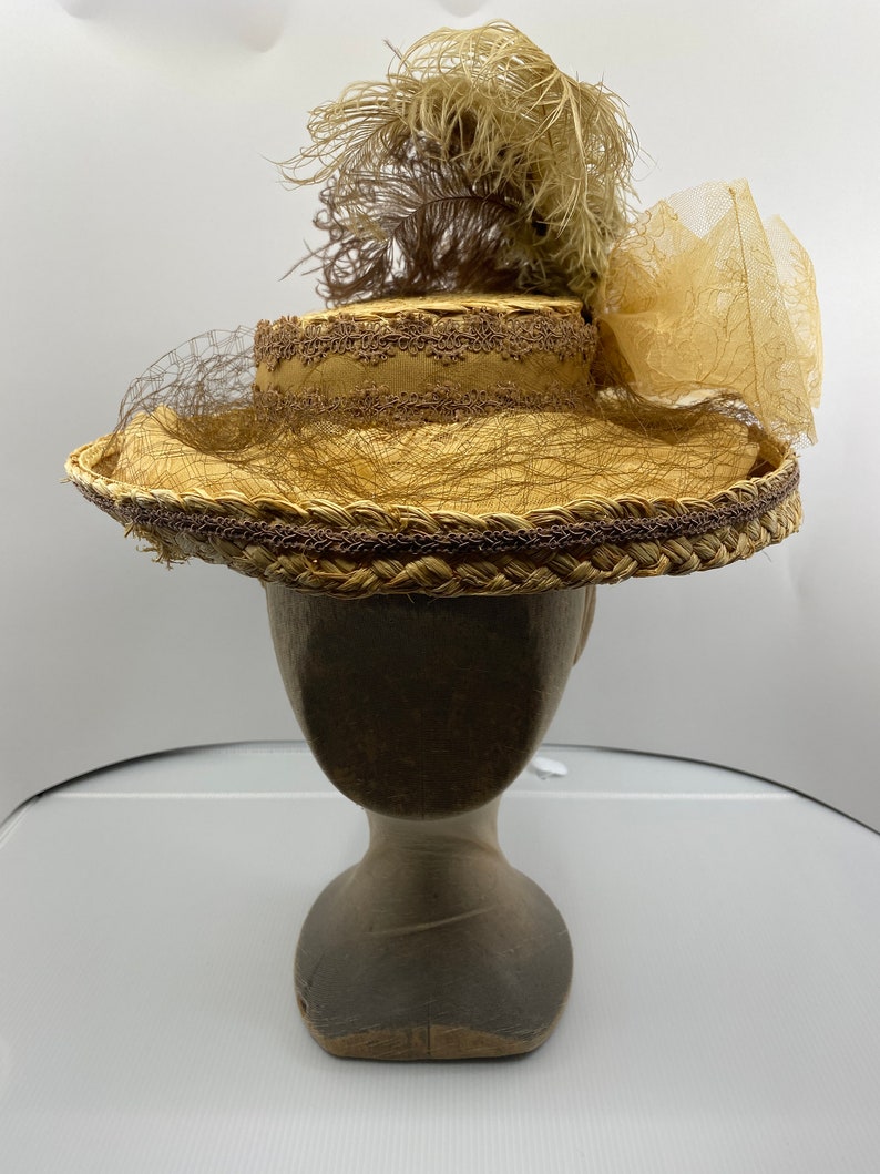 May include: A straw hat with a brown ribbon and a brown feather. The hat is on a wooden hat form.