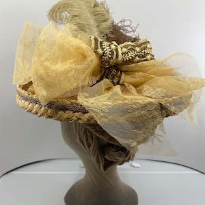 May include: A straw hat with a brown ribbon and a beige feather. The hat is decorated with a large bow made of beige lace.