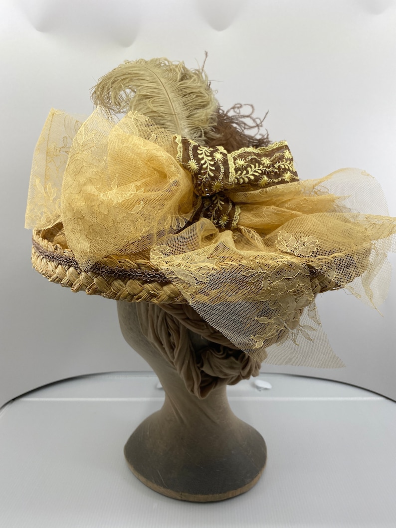 May include: A straw hat with a brown ribbon and a beige feather. The hat is decorated with a large bow made of beige lace.