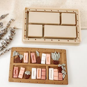 May include: A brown silicone mold with four rectangular cavities for making resin crafts. The mold is shown next to a finished resin piece with a bookshelf design featuring small potted plants, books, and a vase.