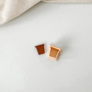 May include: Two plastic plant pot cookie cutters, one brown and one light pink. The cutters are on a white surface.