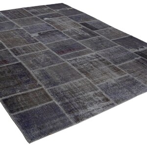 May include: A rectangular patchwork rug in shades of gray, blue, and brown. The rug is composed of numerous rectangular pieces stitched together, creating a textured surface. The rug has a distressed, vintage appearance.