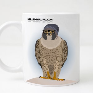 May include: White ceramic mug featuring a black and white illustration of a falcon wearing a blue beanie and black glasses. The text "Millennial Falcon" is printed on the mug.