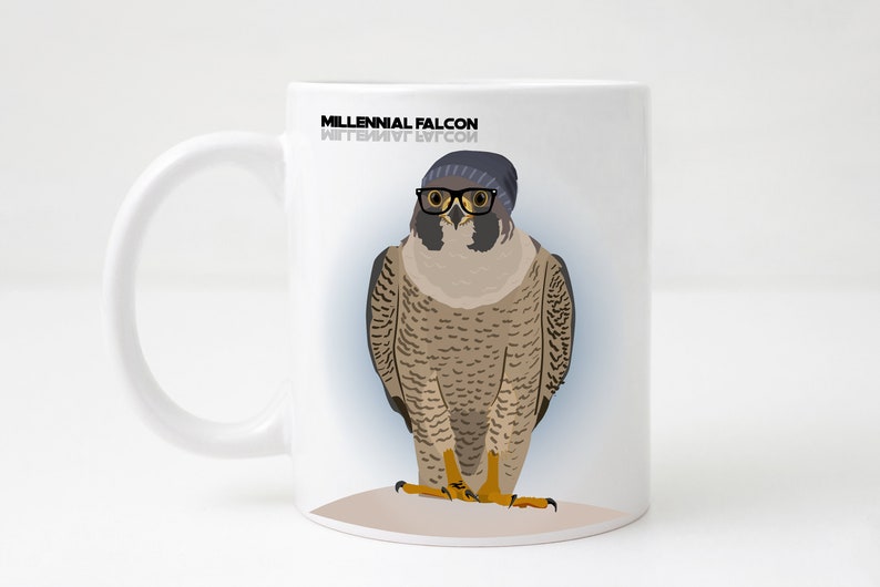 May include: White ceramic mug featuring a black and white illustration of a falcon wearing a blue beanie and black glasses. The text "Millennial Falcon" is printed on the mug.