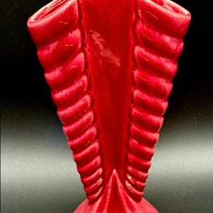 May include: A red ceramic vase with a unique, ribbed design. The vase has a wide opening and a narrow base.