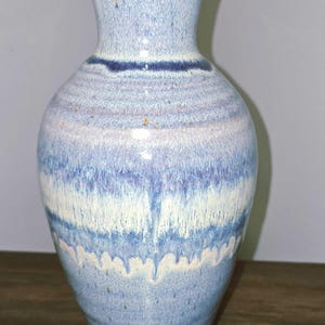 May include: A tall, ceramic vase with a flared top and a wide base. The vase features a blue and white color scheme with horizontal bands of color. The vase is approximately 12 inches tall.