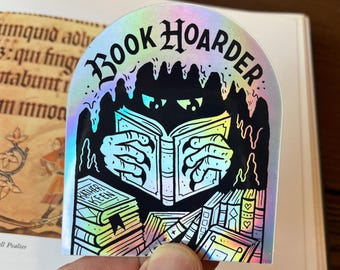 May include: Holographic sticker with the text "BOOK HOARDER" above a black silhouette of a creature reading a book. The sticker features a stack of books with the title "FATHER KEEN" and other book-themed illustrations.
