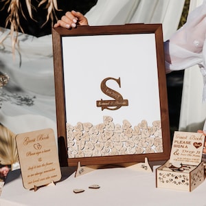 Puede incluir: Alternativa de libro de visitas de madera con marco marrón oscuro, monograma y corazones de madera. Incluye un pequeño letrero de madera y una caja para que los invitados firmen y dejen caer corazones. Decoración de boda.