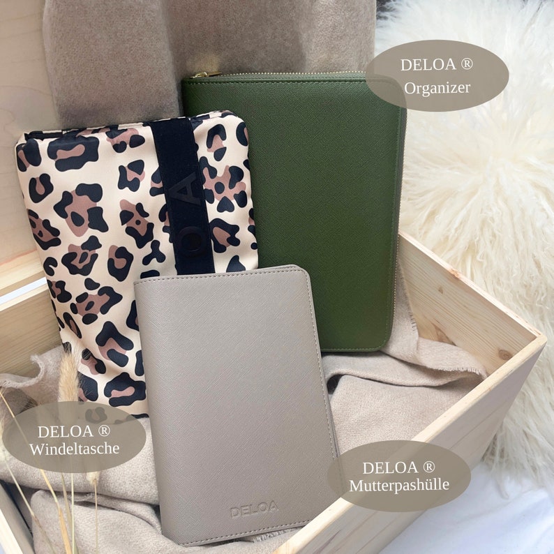 Puede incluir: Tres estuches de cuero con cremallera de diferentes tama&ntilde;os en una caja de madera. Los estuches son en tonos de verde, gris y marr&oacute;n con estampado de leopardo. Los estuches est&aacute;n etiquetados como "DELOA Organizer", "DELOA Windeltasche" y "DELOA Mutterpasch&uuml;lle".