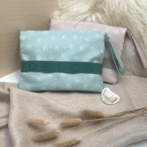 Puede incluir: Una bolsa de cremallera azul claro con un patr&oacute;n de caballo de balanc&iacute;n blanco y la palabra "DELOA" impresa en una correa verde. La bolsa est&aacute; sobre una superficie peluda de color marr&oacute;n claro.
