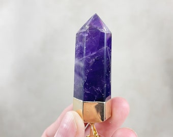 May include: A purple amethyst crystal point pendant with a gold-toned setting and chain. The crystal is faceted and has a pointed tip.