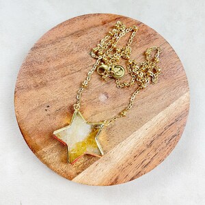 Peut inclure: Un collier en chaîne dorée avec un grand pendentif en forme d'étoile en agate claire et jaune. Le pendentif est serti d'or et pend à une délicate chaîne dorée.