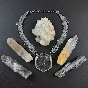 May include: A silver dragon necklace with a clear quartz crystal pendant and five clear quartz crystals. The necklace is on a black background.