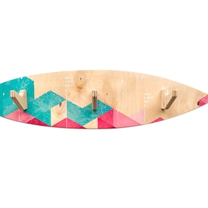 May include: A wooden surfboard-shaped coat rack with a geometric pattern in pink and turquoise. The rack has three hooks and the text "Good Vibes Only" and "Have a Nice Day" printed on it.