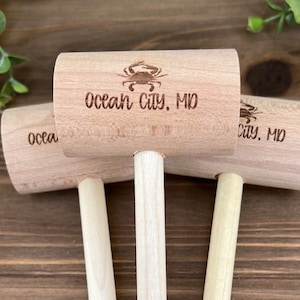 May include: Three wooden crab mallets with a crab design and the text "Ocean City, MD" on the top. The mallets are on a wooden surface.