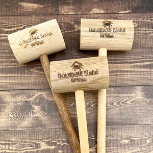 Puede incluir: Tres mazos de madera con mango de madera marrón. Cada mazo tiene el texto "Chincoteague Island Virginia" grabado en la cabeza.