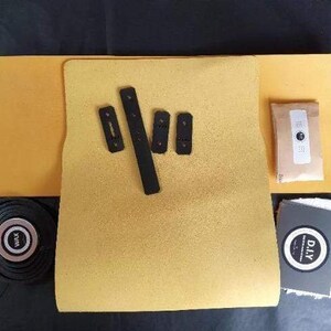 May include: A DIY kit for making a custom skateboard grip tape. The kit includes a sheet of yellow grip tape, black grip tape strips, and a small packet of sandpaper. The kit also includes a small white cloth with the word "DIY" printed on it.
