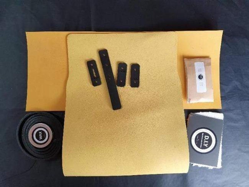 May include: A DIY kit for making a custom skateboard grip tape. The kit includes a sheet of yellow grip tape, black grip tape strips, and a small packet of sandpaper. The kit also includes a small white cloth with the word "DIY" printed on it.