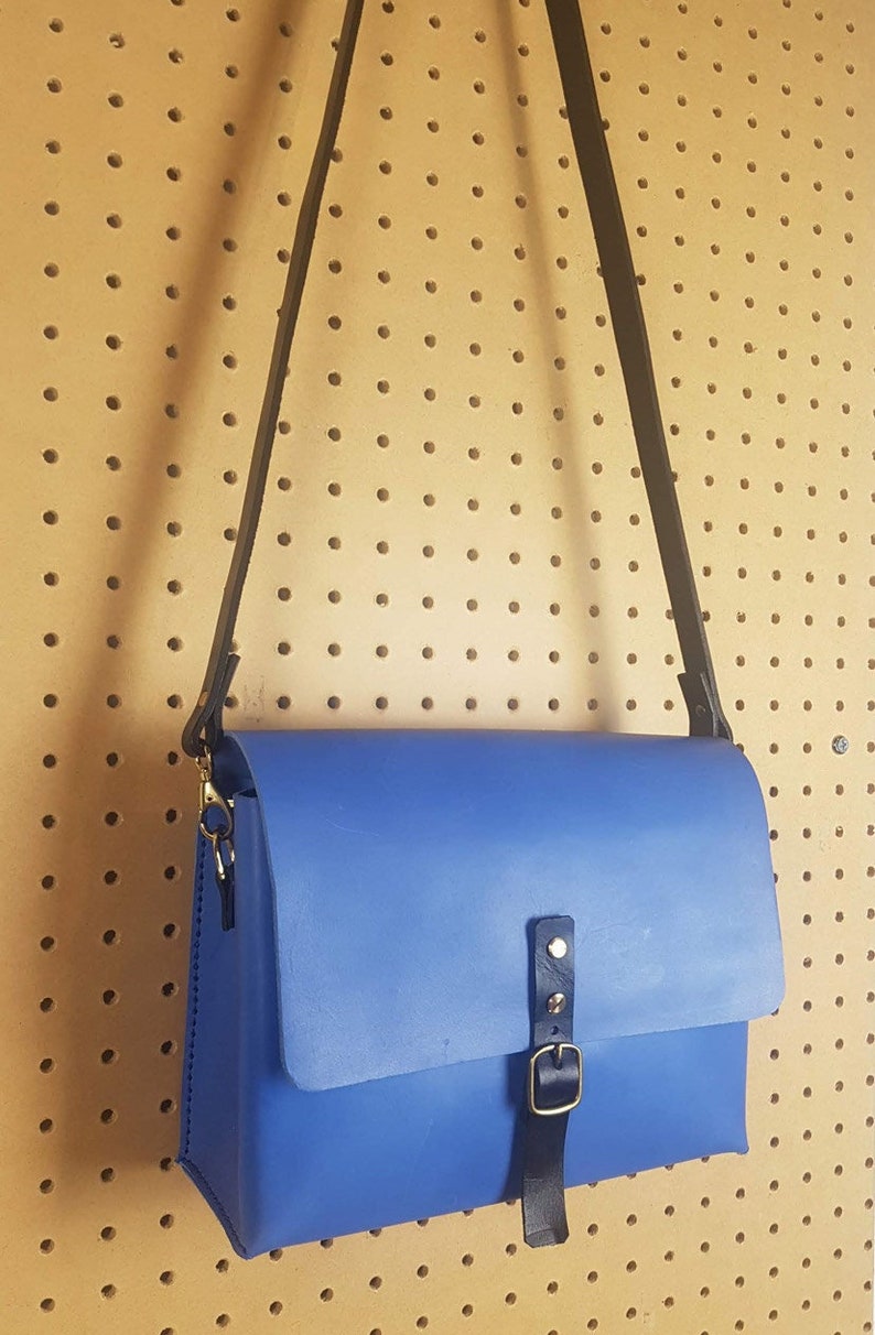 May include: A blue leather crossbody bag with a black strap and a gold buckle.