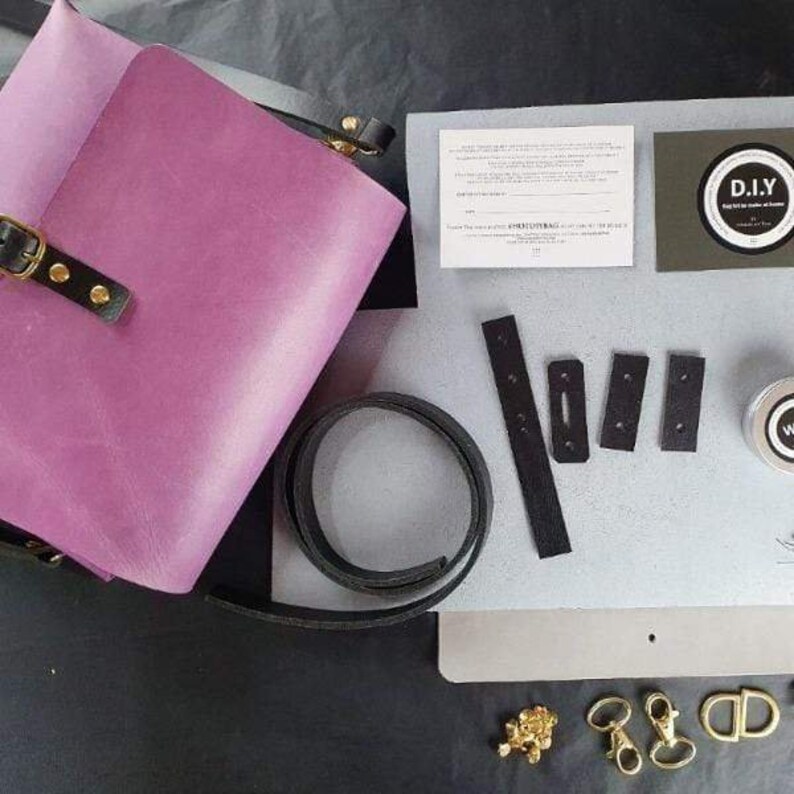 May include: A DIY leather bag kit featuring a purple leather bag, black leather straps, and gold hardware. The kit also includes instructions and a small jar of leather conditioner.