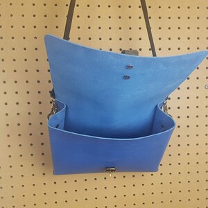 May include: A blue leather satchel bag with a flap closure and a strap. The bag is open and the inside is visible.