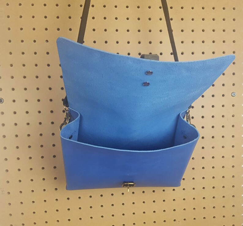 May include: A blue leather satchel bag with a flap closure and a strap. The bag is open and the inside is visible.