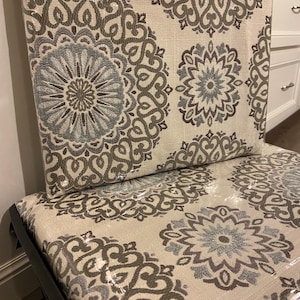 Puede incluir: Silla tapizada con tela color crema con un patr&oacute;n repetido de medallones florales grises y azules. La silla tiene una estructura negra y est&aacute; cubierta con envoltura de pl&aacute;stico.