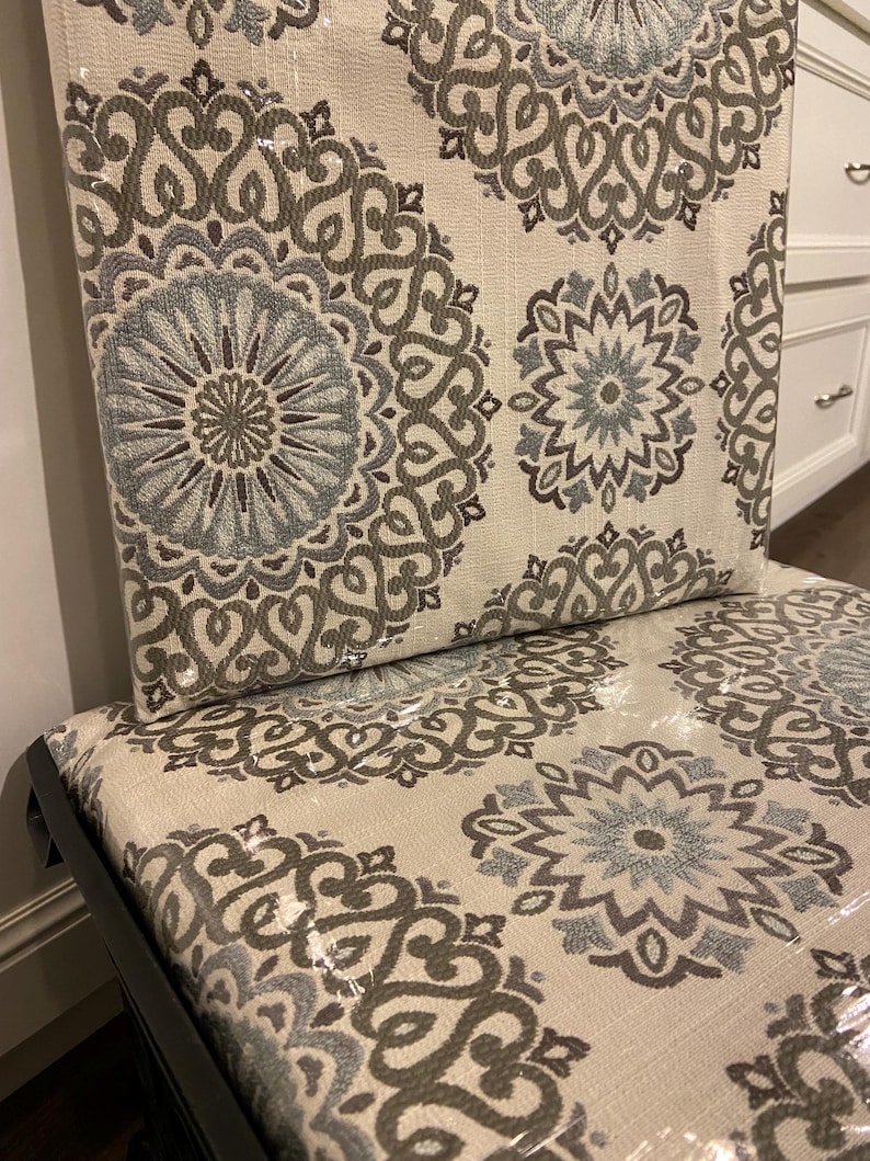 Puede incluir: Silla tapizada con tela color crema con un patr&oacute;n repetido de medallones florales grises y azules. La silla tiene una estructura negra y est&aacute; cubierta con envoltura de pl&aacute;stico.