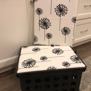Puede incluir: Una caja de almacenamiento de pl&aacute;stico negro con un coj&iacute;n blanco con un patr&oacute;n de diente de le&oacute;n negro. Una toalla a juego con el mismo patr&oacute;n cuelga de una puerta de armario blanca. La caja est&aacute; sobre una alfombra gris.