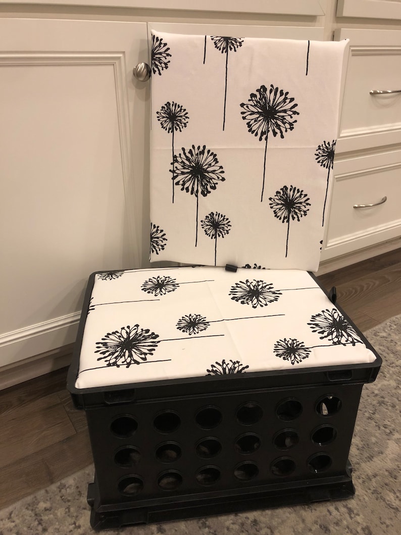 Puede incluir: Una caja de almacenamiento de pl&aacute;stico negro con un coj&iacute;n blanco con un patr&oacute;n de diente de le&oacute;n negro. Una toalla a juego con el mismo patr&oacute;n cuelga de una puerta de armario blanca. La caja est&aacute; sobre una alfombra gris.