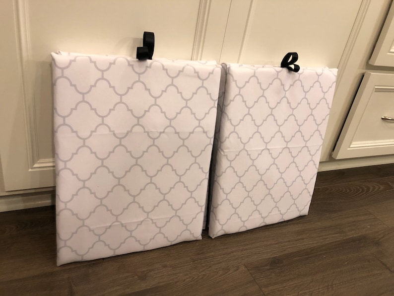 Puede incluir: Dos bolsas de almacenamiento de tela blanca con un patr&oacute;n de cuadrifolio gris. Cada bolsa tiene un lazo negro en la parte superior para colgar. Las bolsas est&aacute;n apoyadas contra un armario blanco.