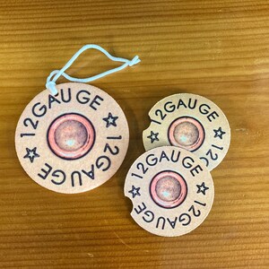 May include: Three brown and white round coasters with the text "12 Gauge" printed on them. The coasters have a star design and a red circle in the center.