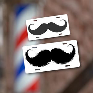 May include: Two white license plate-style signs with black mustache designs. The top sign has a simple mustache, while the bottom sign has a more detailed, bushy mustache.
