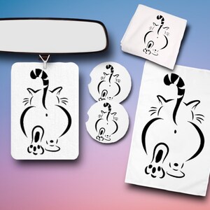 May include: A set of cat-themed home goods featuring a black and white silhouette of a cat's rear end. The set includes a car air freshener, two coasters, a hand towel, and a tea towel.