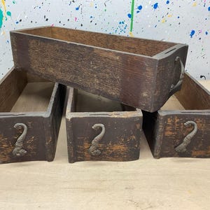 May include: A collection of five weathered wooden boxes. The boxes are rectangular with a dark brown finish and ornate metal handles. The wood shows signs of age and wear, adding to their rustic charm.