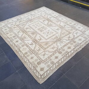 Puede incluir: Una alfombra blanca con un patr&oacute;n geom&eacute;trico marr&oacute;n. La alfombra tiene un medall&oacute;n central con un patr&oacute;n repetitivo de flores y hojas estilizadas.