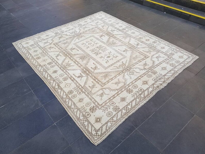 Puede incluir: Una alfombra blanca con un patr&oacute;n geom&eacute;trico marr&oacute;n. La alfombra tiene un medall&oacute;n central con un patr&oacute;n repetitivo de flores y hojas estilizadas.