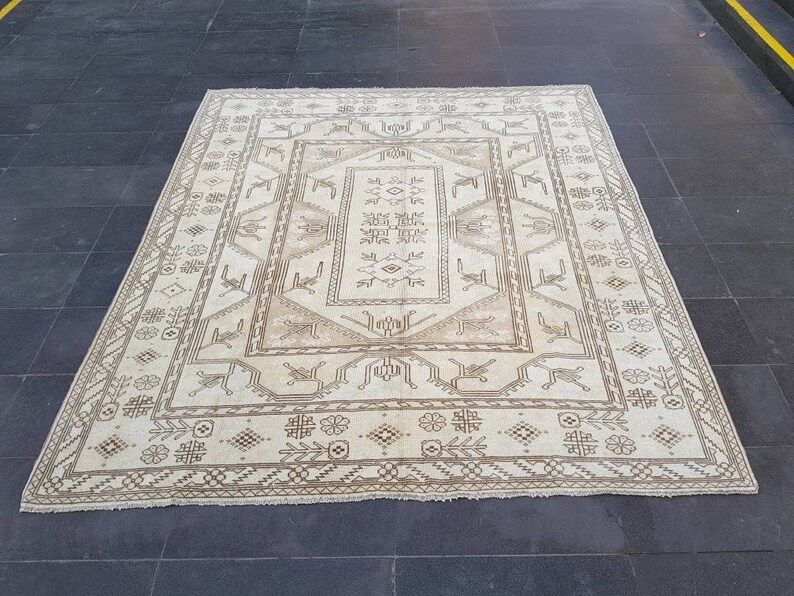 Puede incluir: Una alfombra de color crema con un patr&oacute;n geom&eacute;trico marr&oacute;n. La alfombra tiene un medall&oacute;n central con un patr&oacute;n repetitivo de flores y hojas estilizadas.