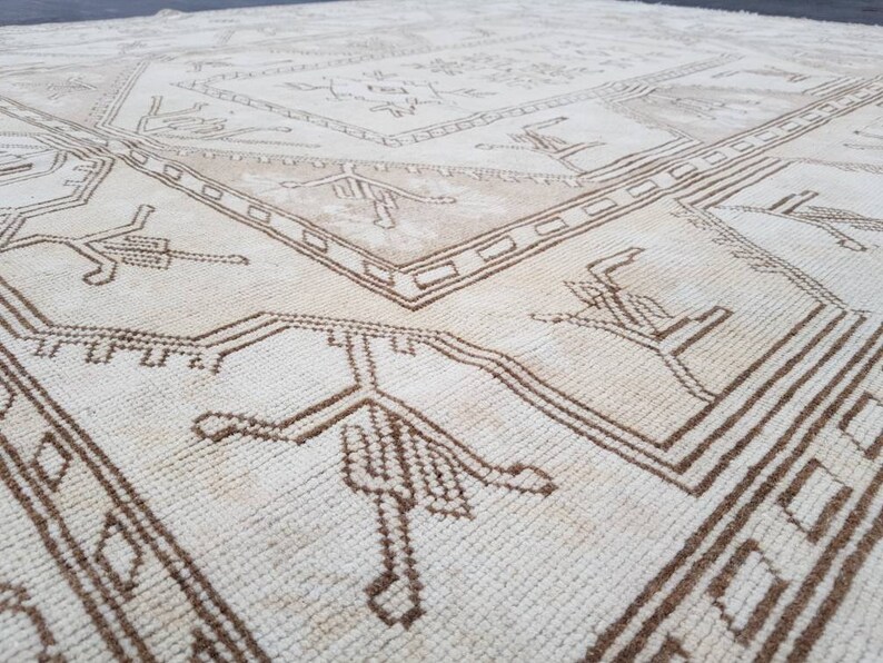 Puede incluir: Una alfombra blanca con un patr&oacute;n geom&eacute;trico marr&oacute;n. El patr&oacute;n presenta dise&ntilde;os repetidos de p&aacute;jaros estilizados y formas geom&eacute;tricas.