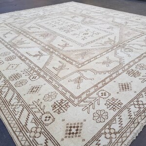 Puede incluir: Una alfombra blanca con un patr&oacute;n geom&eacute;trico marr&oacute;n. La alfombra tiene un aspecto desgastado y est&aacute; hecha de un material suave y tejido.