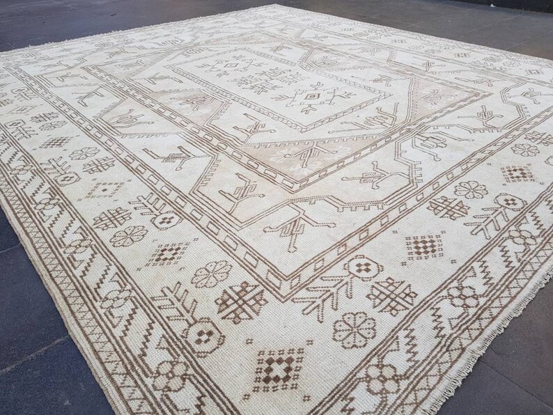 Puede incluir: Una alfombra blanca con un patr&oacute;n geom&eacute;trico marr&oacute;n. La alfombra tiene un aspecto desgastado y est&aacute; hecha de un material suave y tejido.
