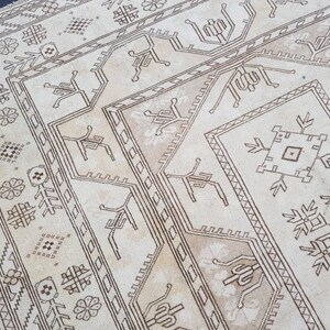 Puede incluir: Una alfombra beige con un patr&oacute;n geom&eacute;trico marr&oacute;n. El patr&oacute;n presenta motivos repetidos de flores estilizadas, estrellas y formas geom&eacute;tricas.